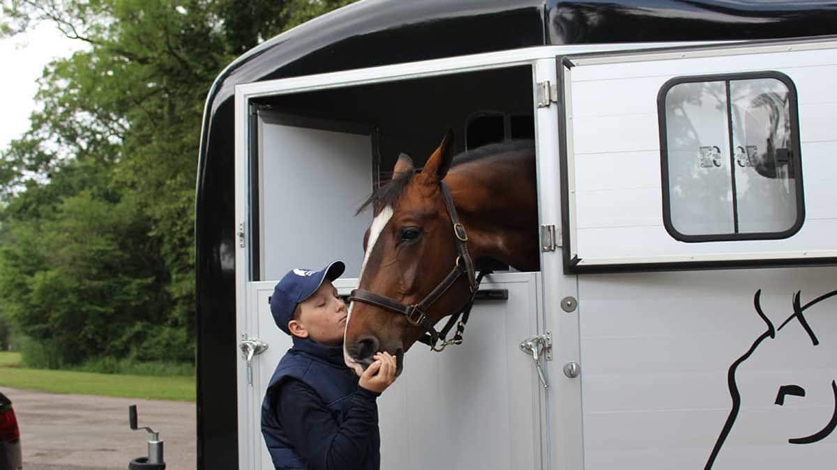 Un cheval passe la tête hors d'un van. Un jeune garçon l'embrasse sur le nez.